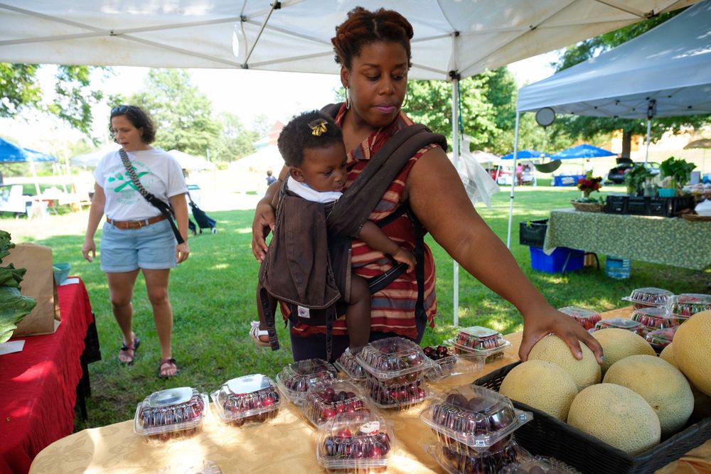 Vendor selling fresh melons and packaged berries at outdoor market stand.