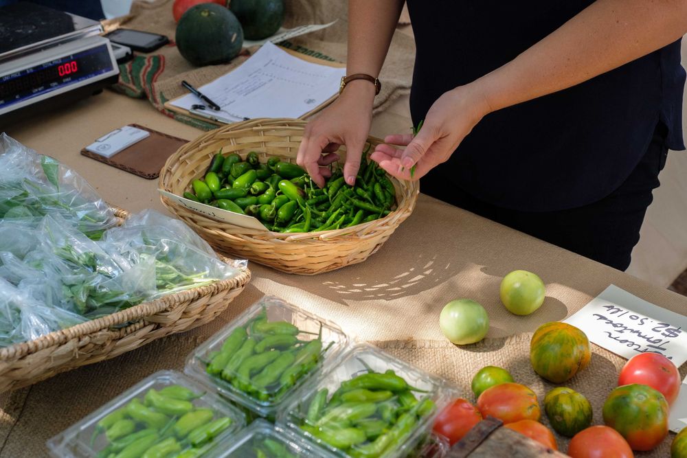 Fresh vegetables and produce being sorted into baskets at farmers market stand.