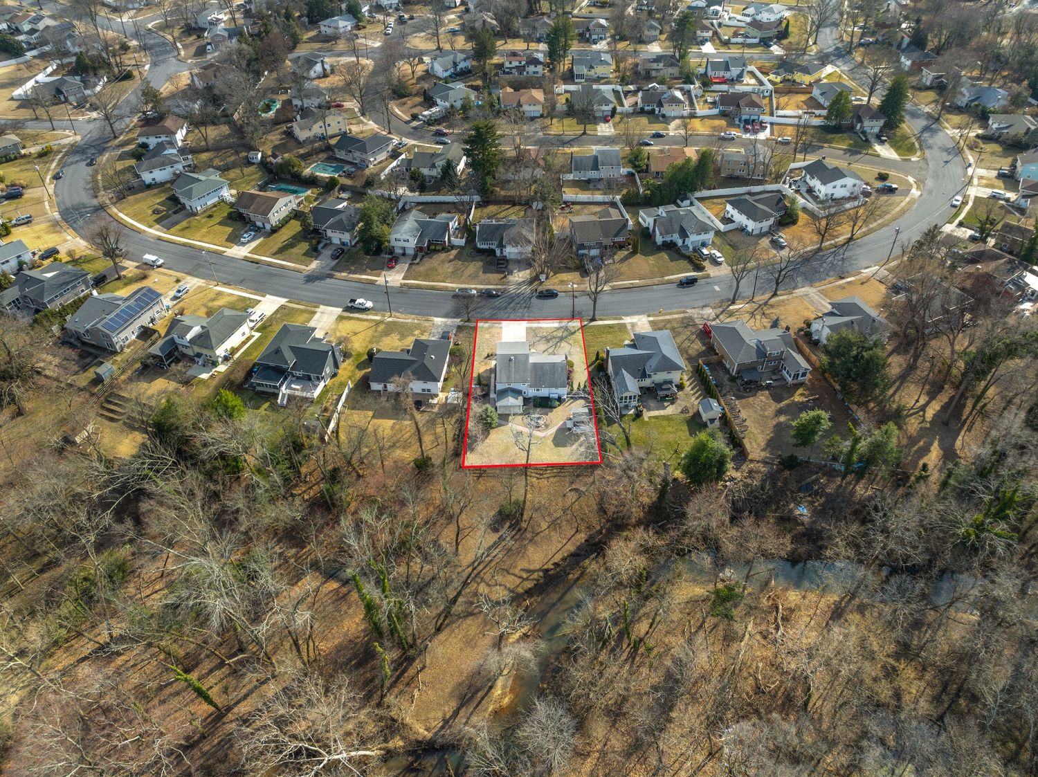 Aerial drone view of a curved suburban street with houses arranged in a horseshoe pattern surrounded by winter trees.
