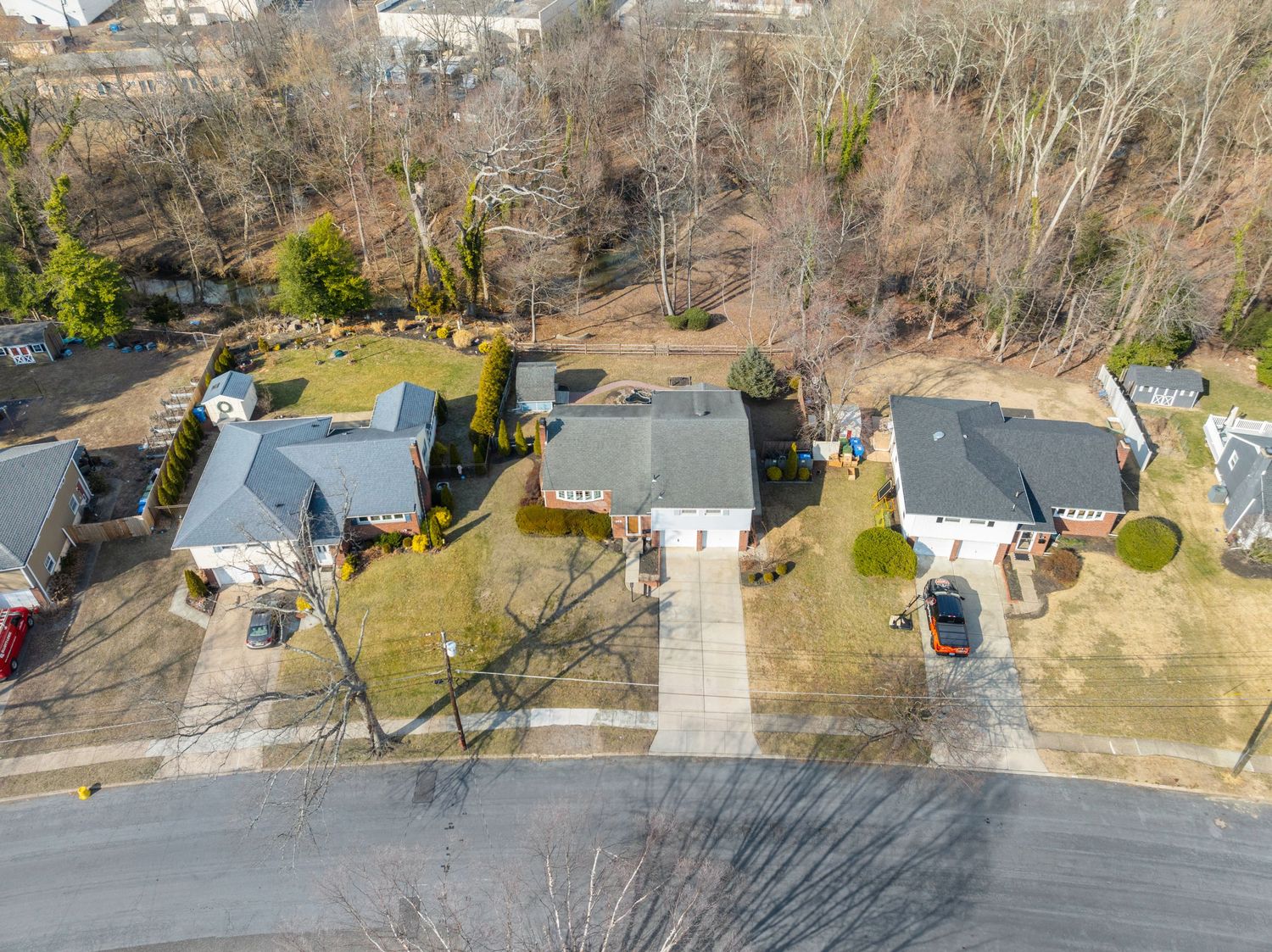 Aerial drone view of suburban homes with gray roofs along a residential street during winter with bare trees.
