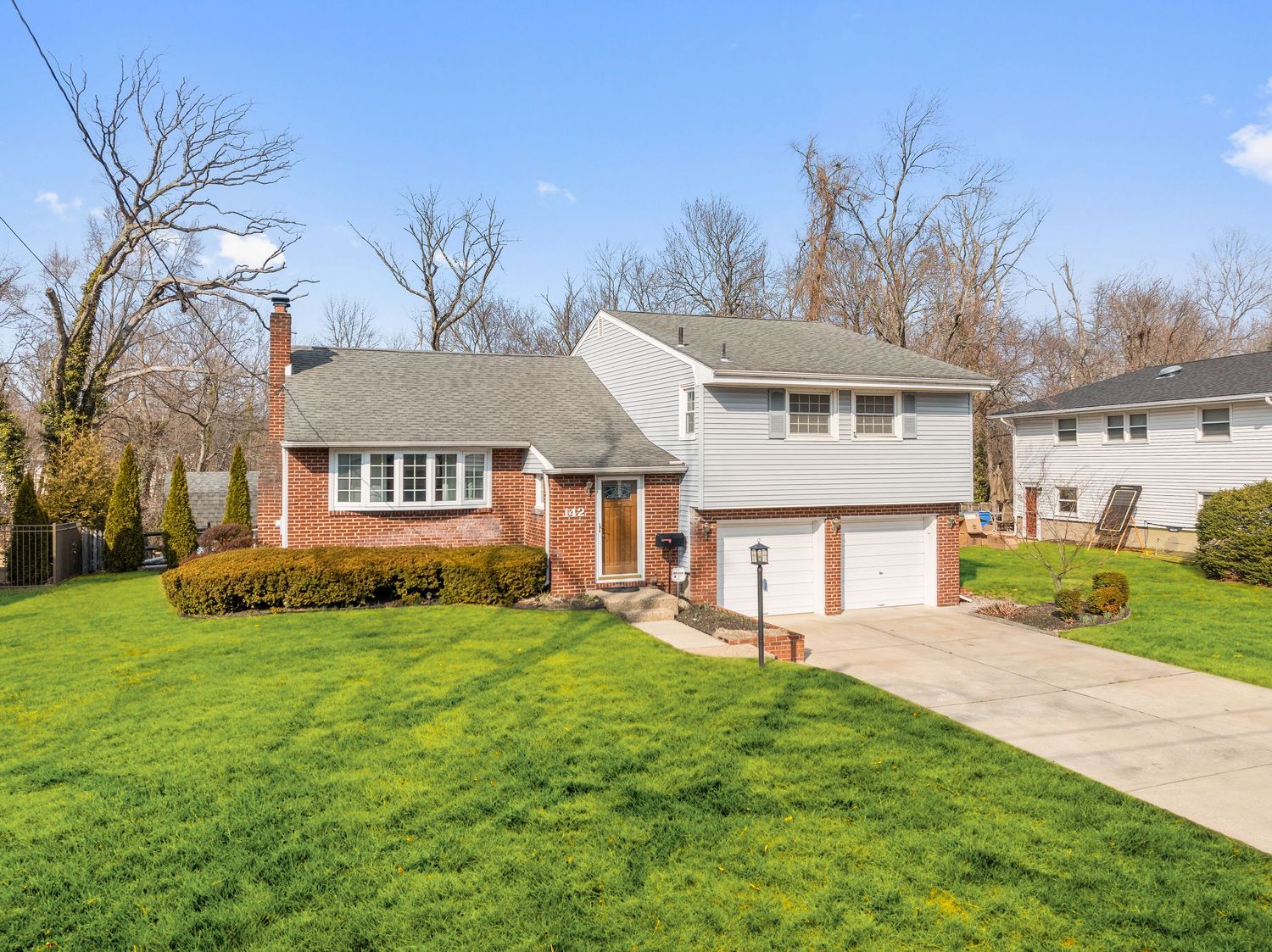 Split-level brick home with attached garage features manicured lawn and bushes on a sunny day.