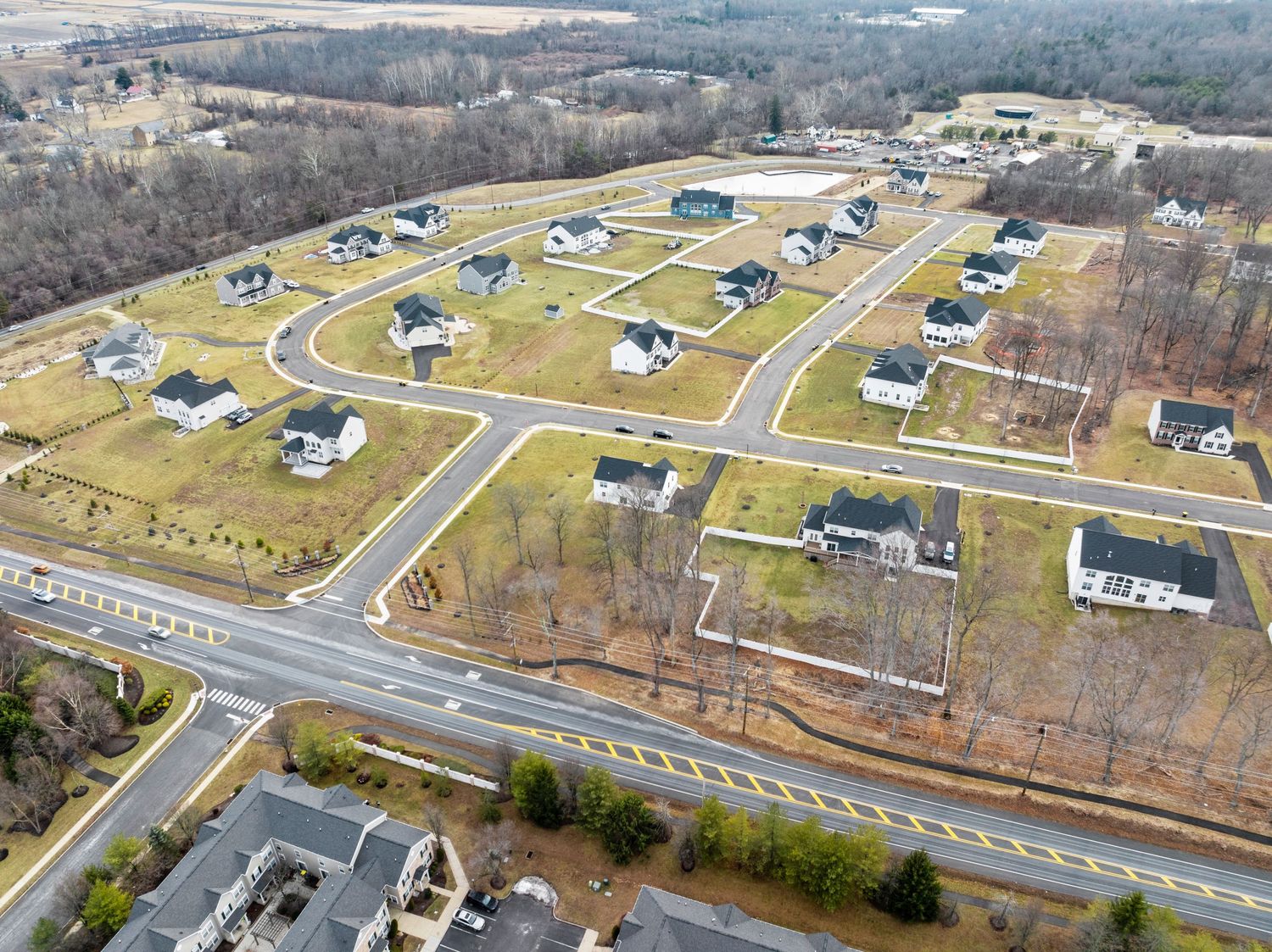 Aerial view of a suburban housing development with curved streets and newly built homes surrounded by woodlands.