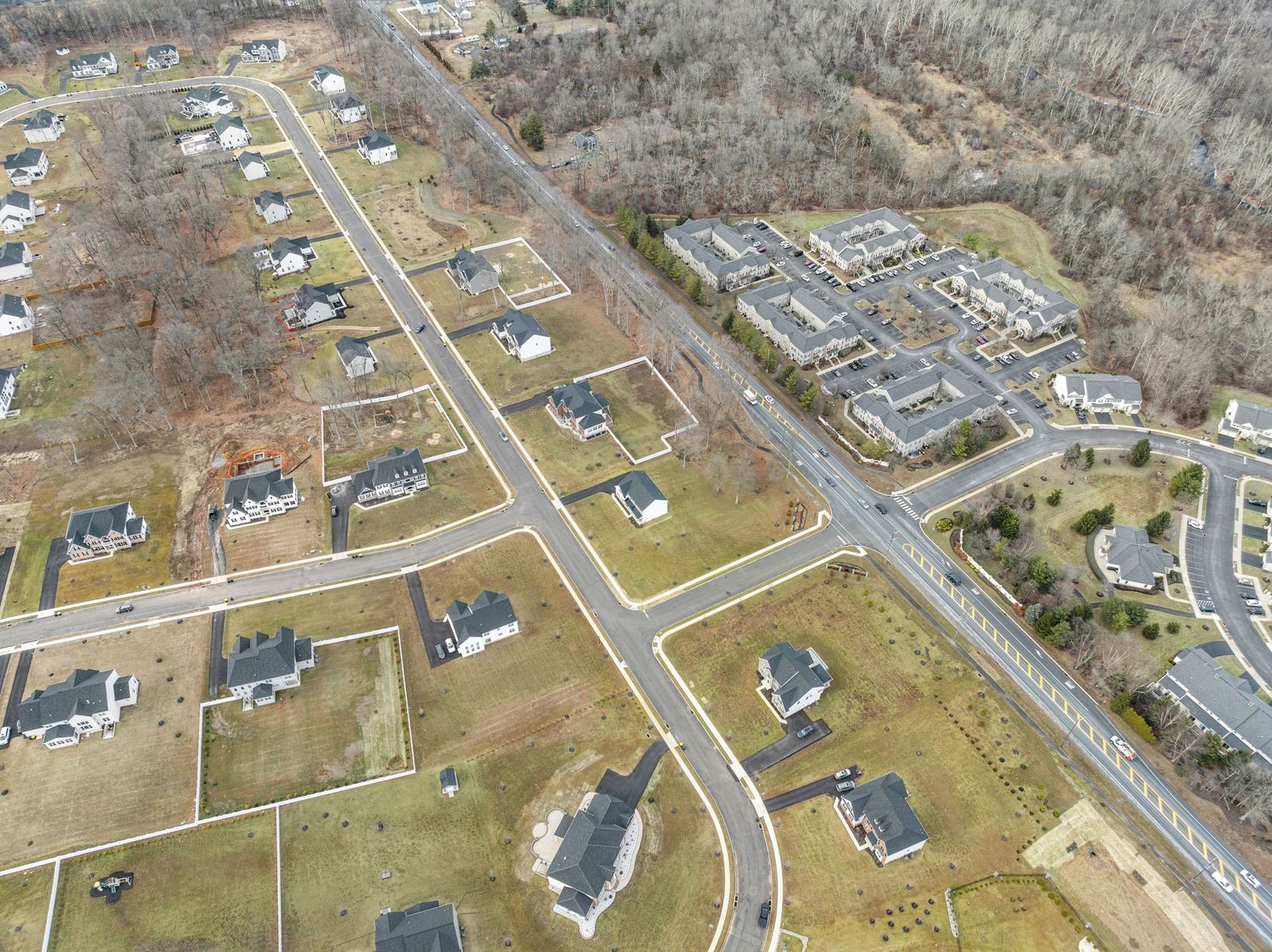 Bird's eye view of a residential subdivision showing paved roads, single family homes, and adjacent developments beyond.