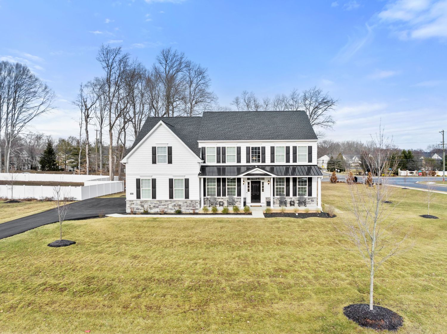 White two-story colonial style house with a front porch and black shutters sits on a spacious green lawn under blue skies.
