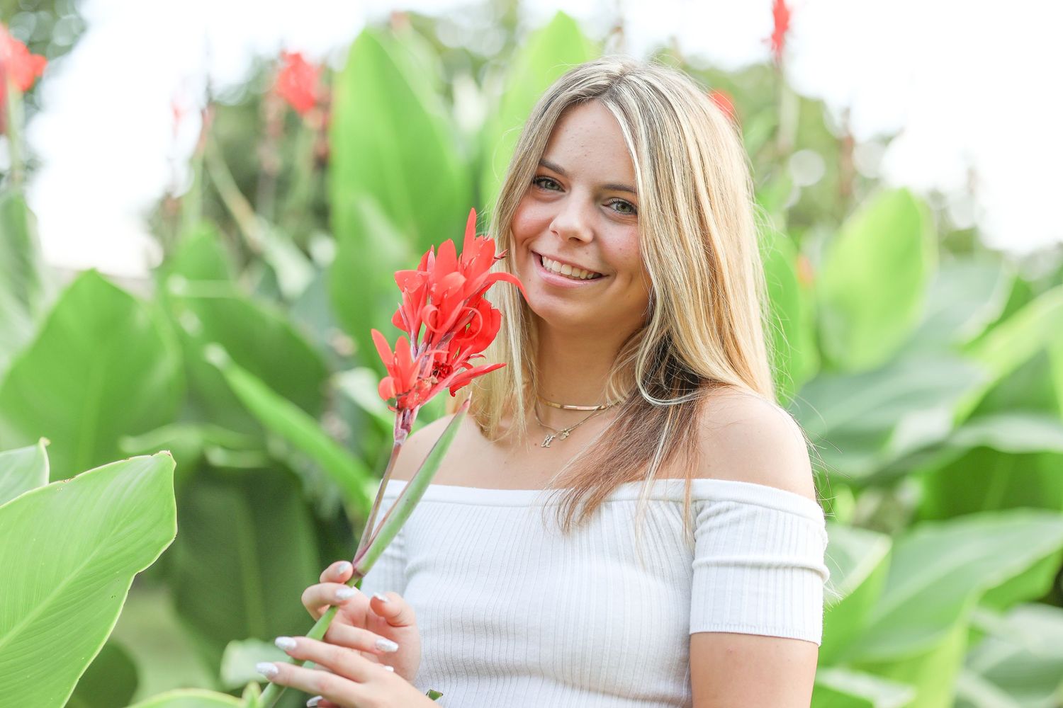 Springfield, IL senior photographer smells a coral color flower during a senior session at Washington Park Botanical Gardens in Central, IL