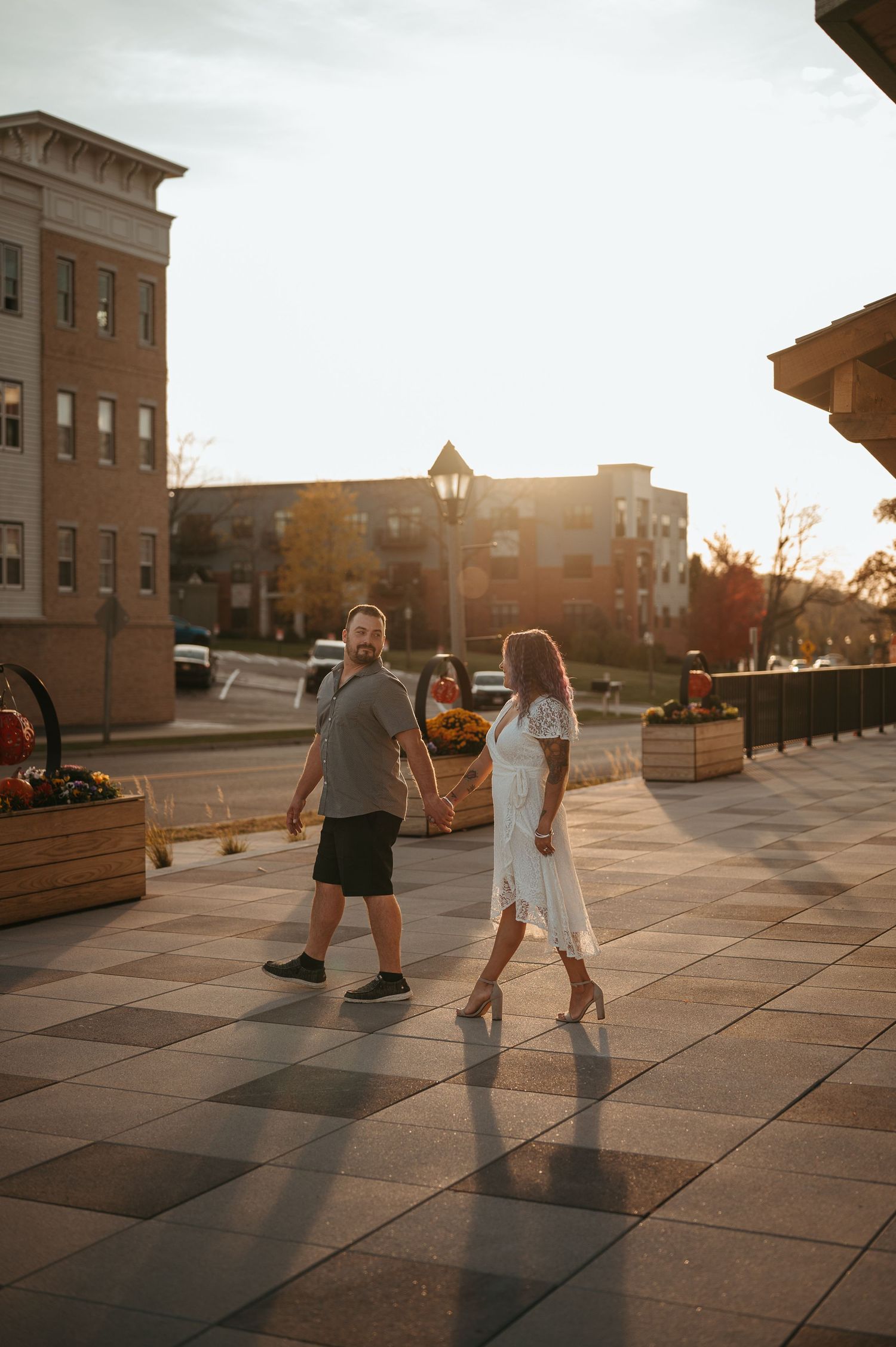 Couple walks through urban setting during sunset with brick buildings in background.