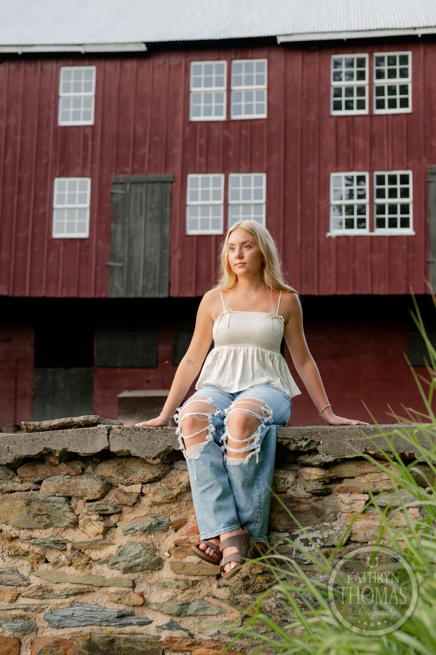Artistic portrait on stone wall with historic red barn backdrop.