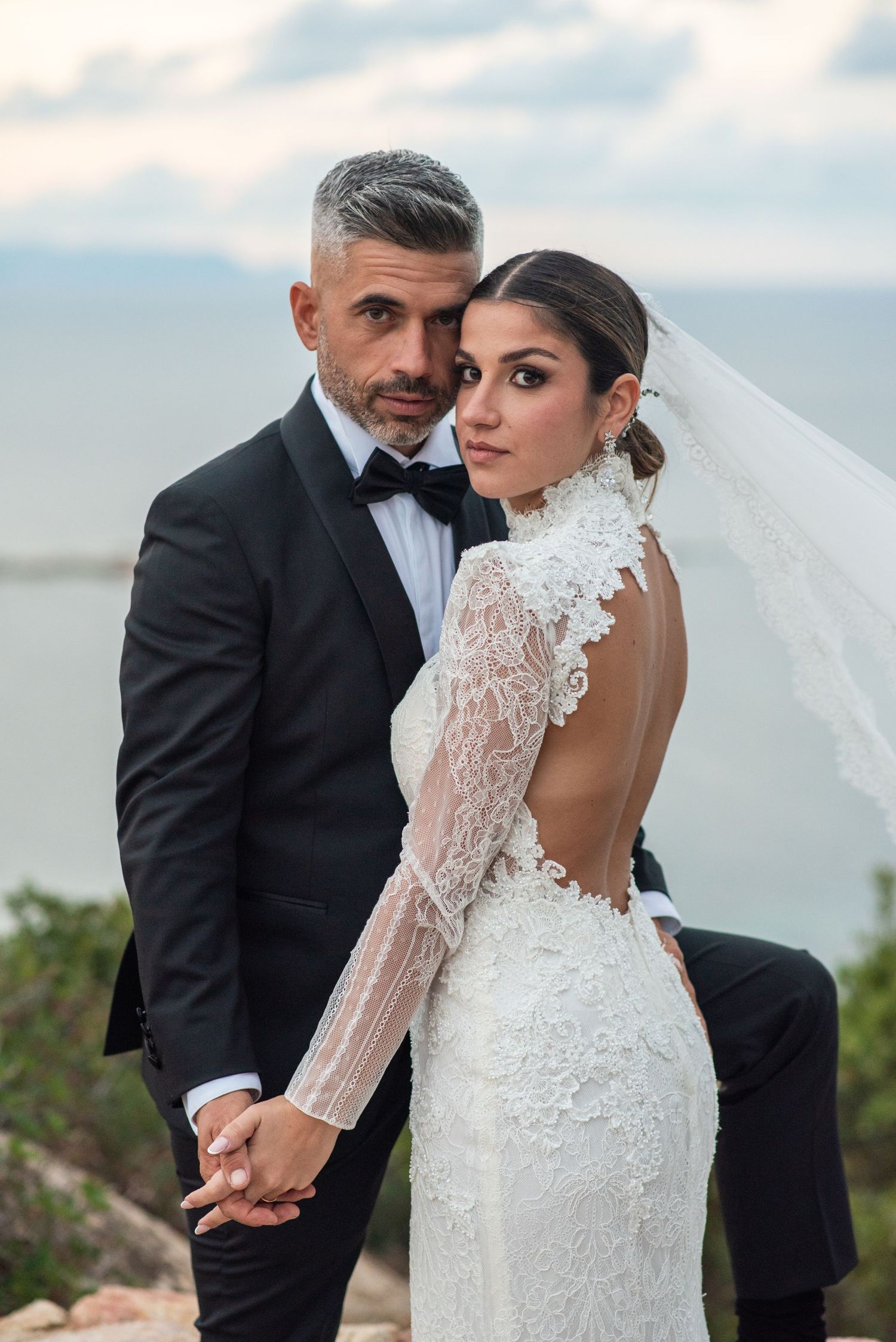 Couple in wedding attire posing together outdoors.