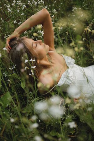 A dreamy outdoor portrait in a wildflower meadow with someone lying in white dress among delicate blooms and greenery.