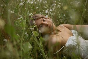 Ethereal portrait of someone lying in a meadow surrounded by delicate white wildflowers and tall green grass.