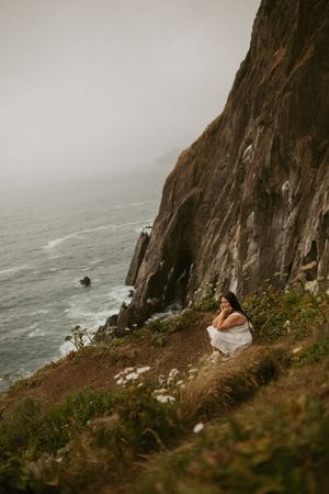 A moody coastal landscape shows rocky cliffs meeting the misty ocean with waves crashing against the rugged shoreline.