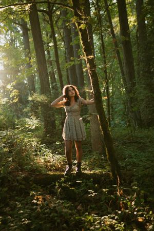 A person in a flowy dress spins joyfully in a sunlit forest clearing surrounded by trees and lush greenery.