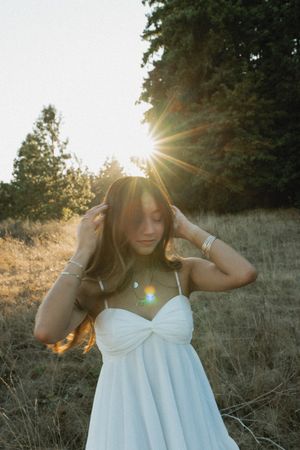A person in a flowing white dress poses outdoors during golden hour sunlight creating a dreamy ethereal effect.