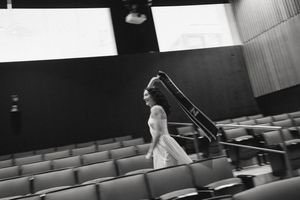 Black and white photo of a woman in a white dress walking through an empty auditorium with tiered seating.
