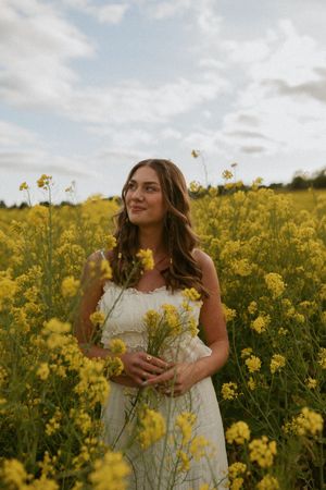 Dreamy summertime portrait in a blooming yellow canola field with a white dress against a cloudy sky.