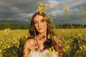 Person poses in white dress among blooming yellow wildflowers during golden hour.