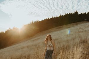 Golden sunset illuminates tall grass on hillside with silhouette of person standing in striped shirt.