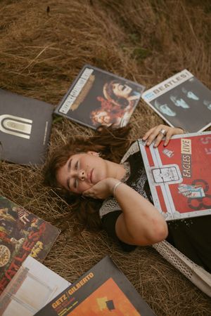 A person lies on the ground surrounded by vinyl records and music albums in a nostalgic setting.