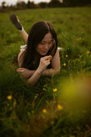 Person lying in grassy field with yellow wildflowers during golden hour.