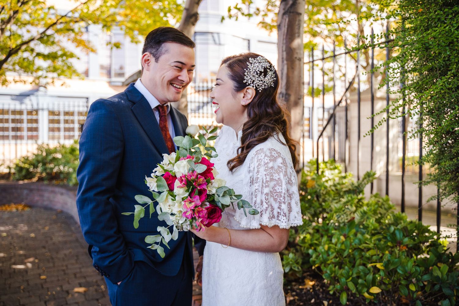 Newlyweds smiling at each other her bouquet has pink and white flowers