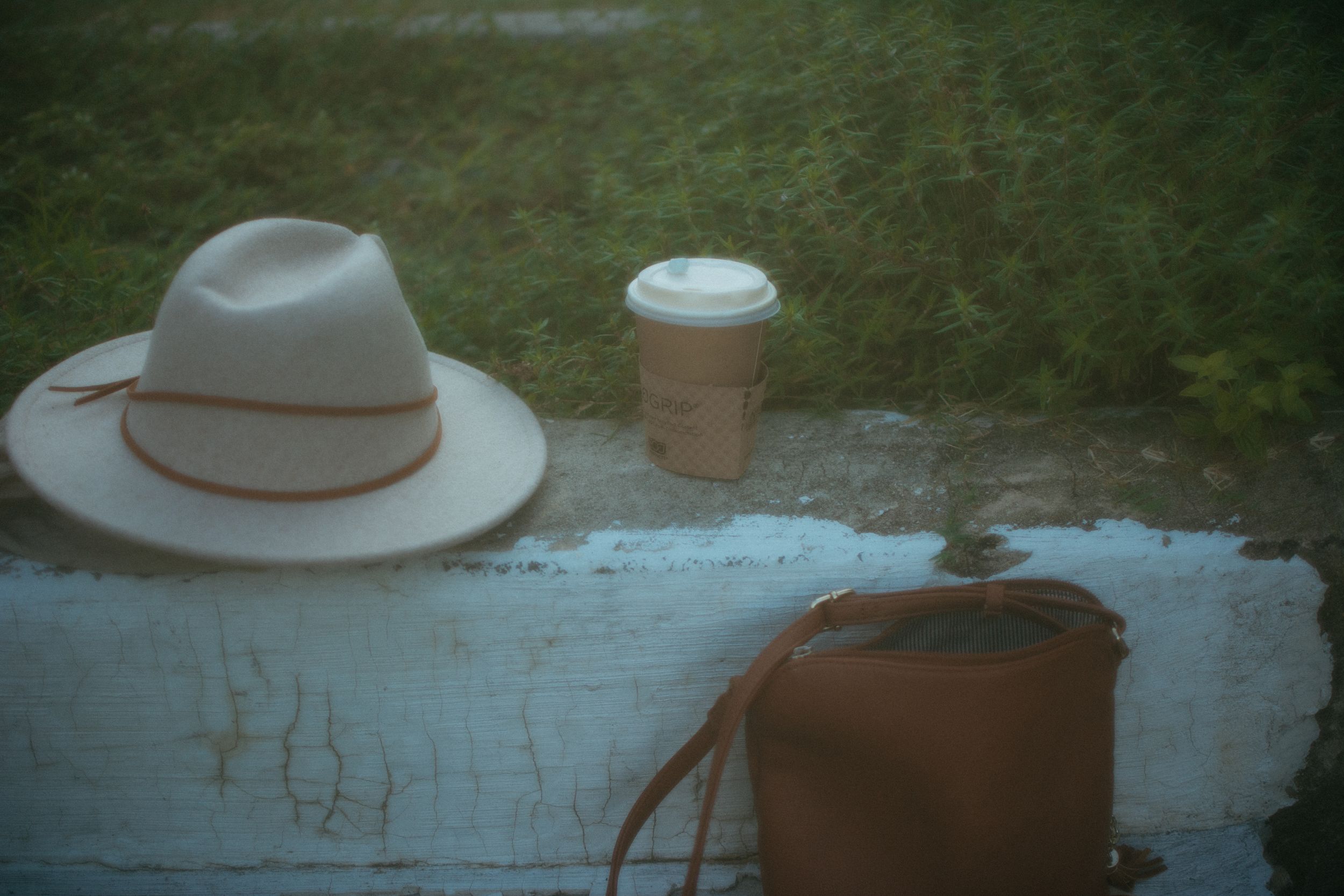 wide brimmed hat, coffe cup, and purse on a grass lined curb