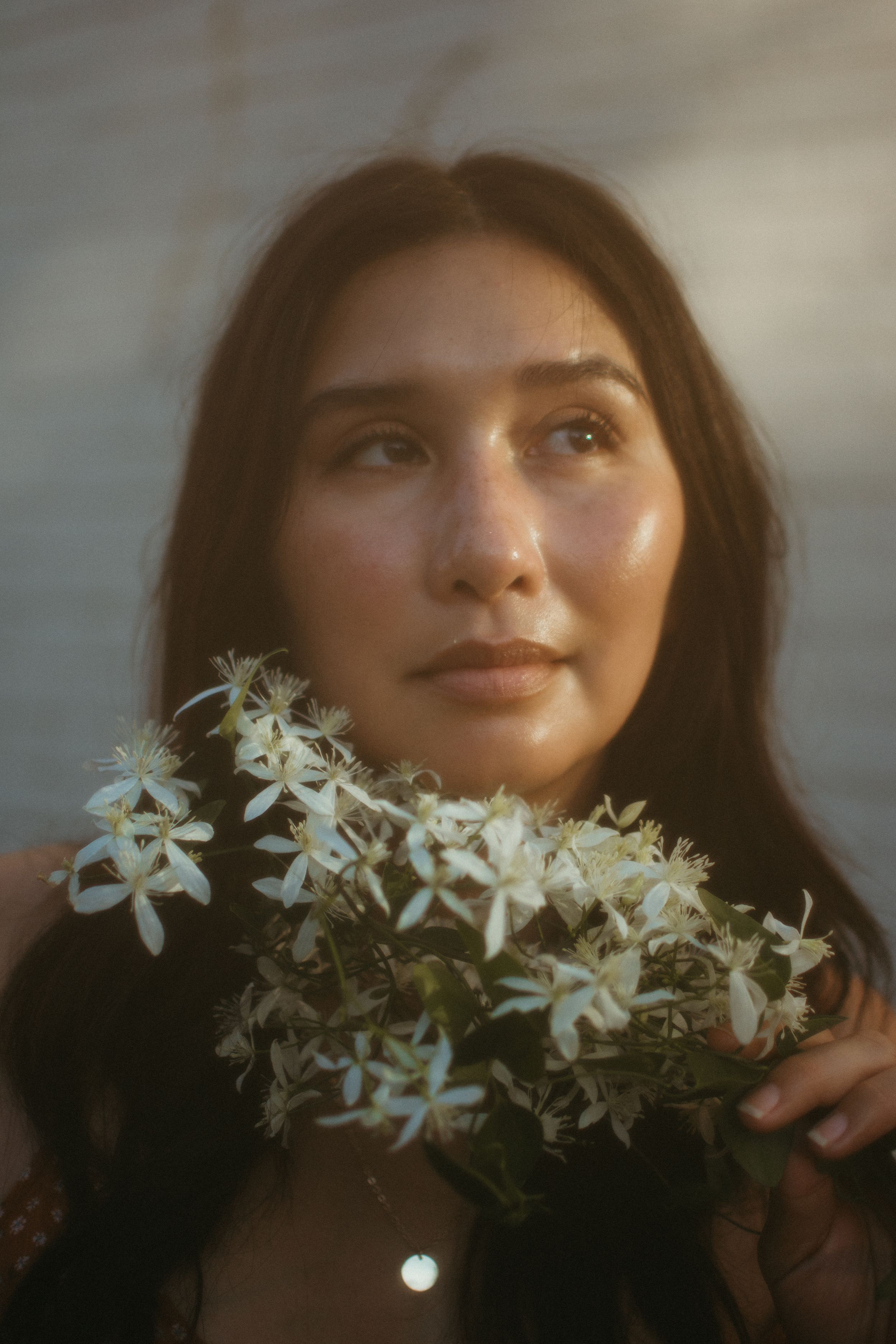 close up photo of brunette woman holding small white flowers under her chin