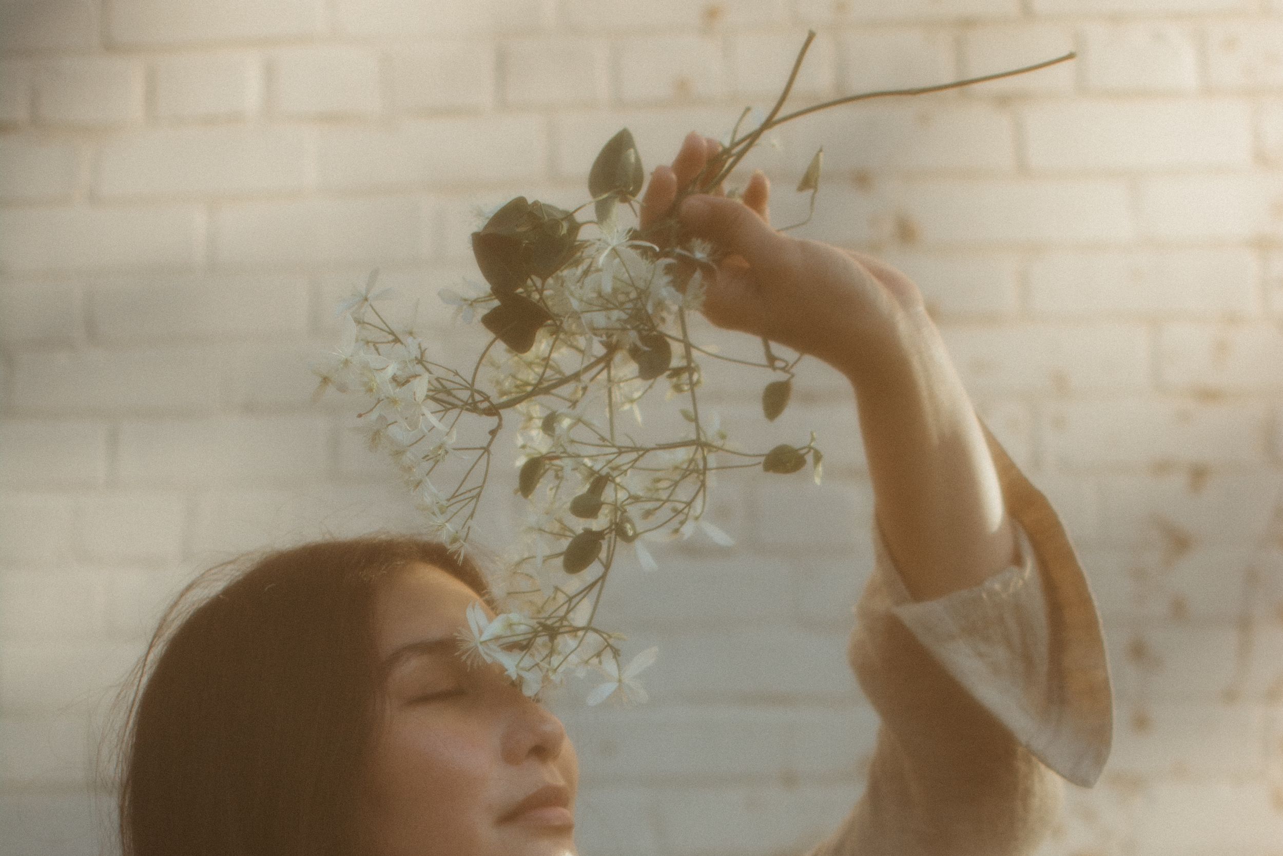 close up photo of brunette woman holding small white flowers up to her face