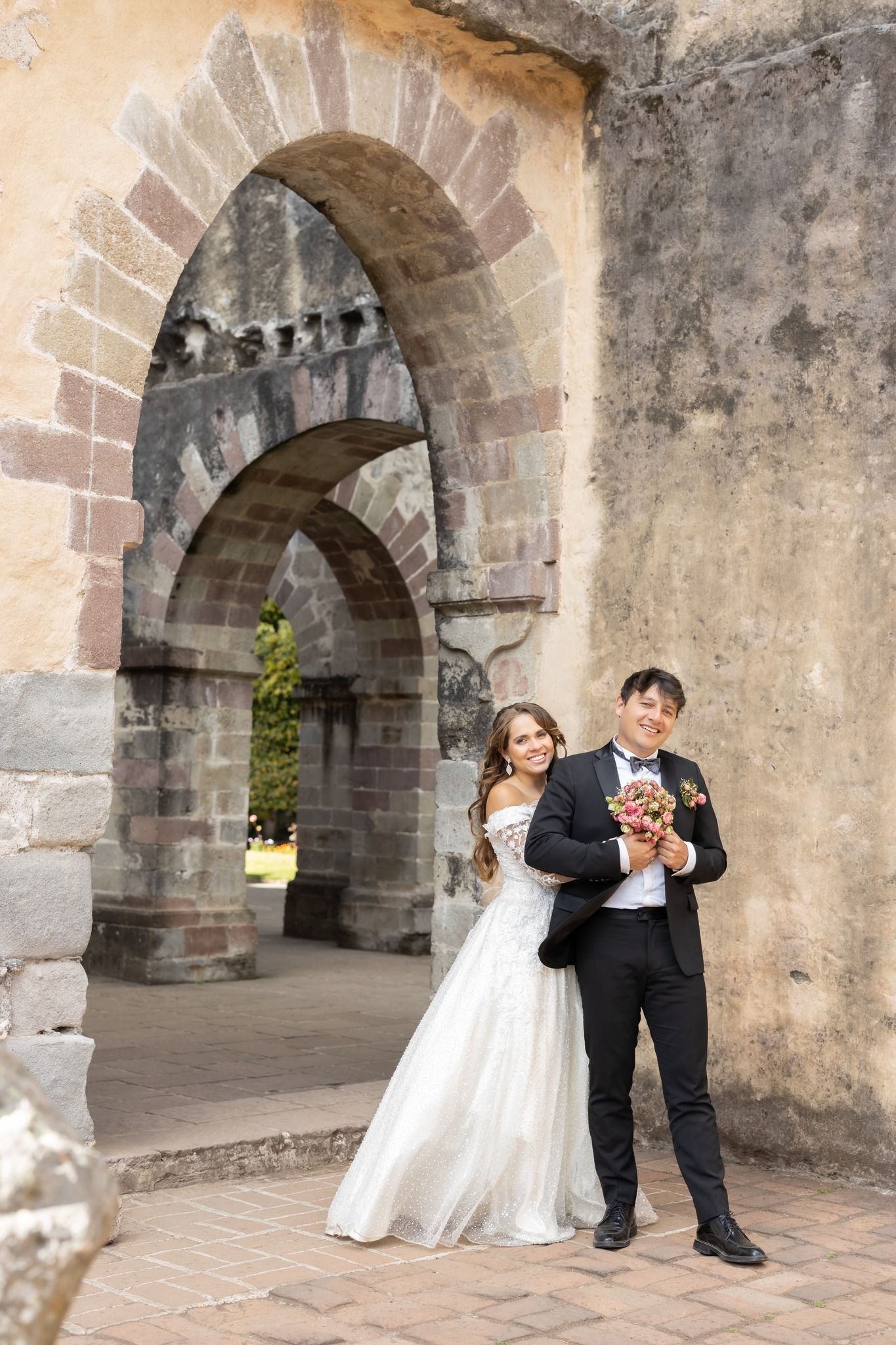 Newlyweds posing under stone arches in elegant wedding attire.