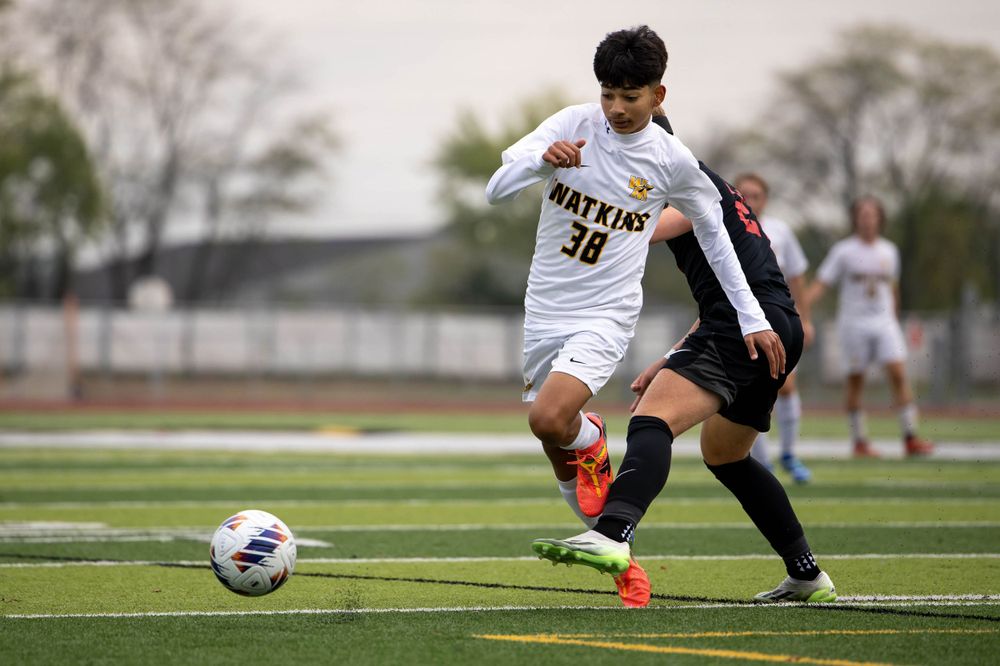 Soccer player in white jersey dribbles ball during competitive match on turf field.