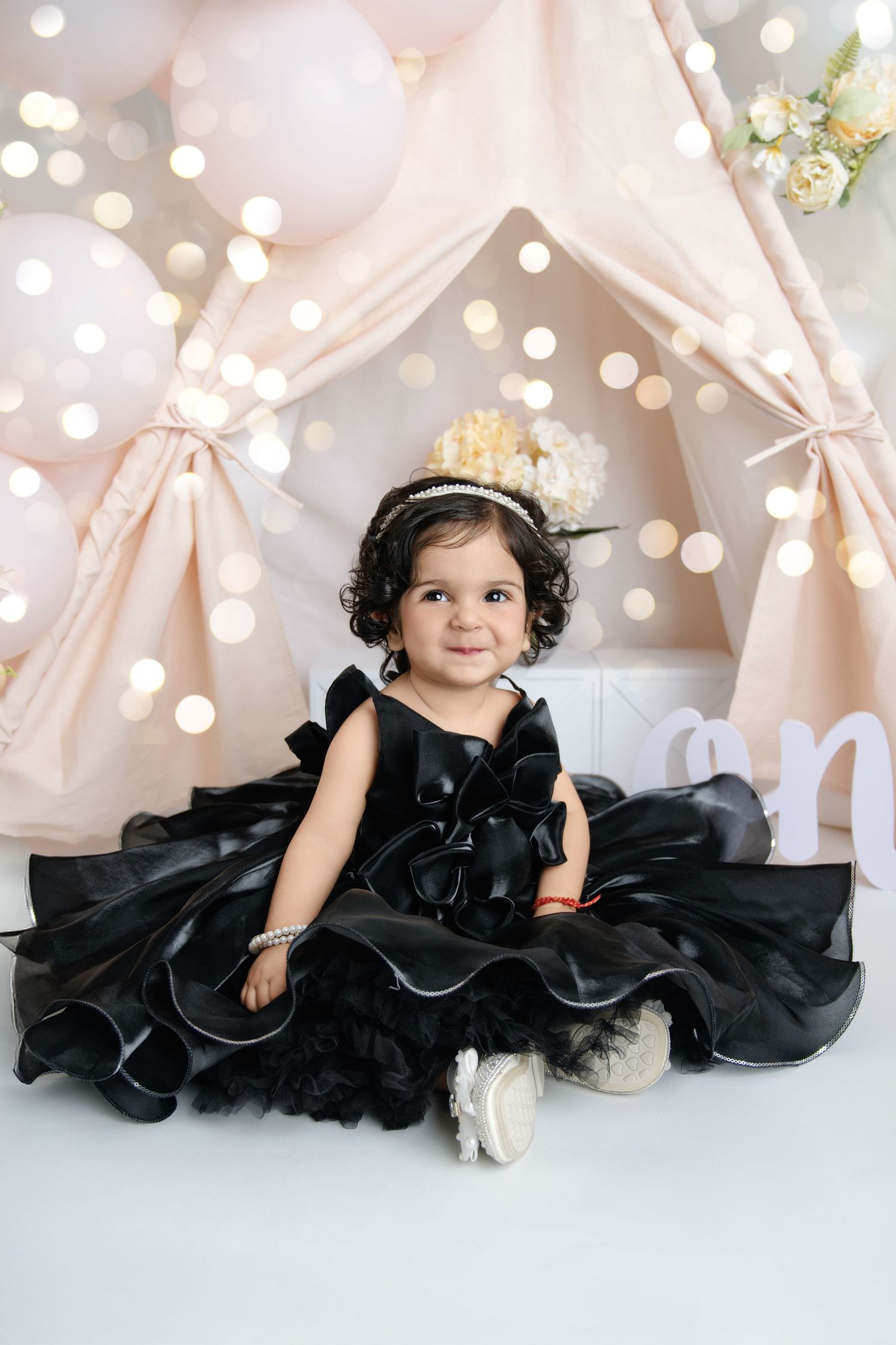 Baby in black tulle dress poses against sparkly light backdrop.