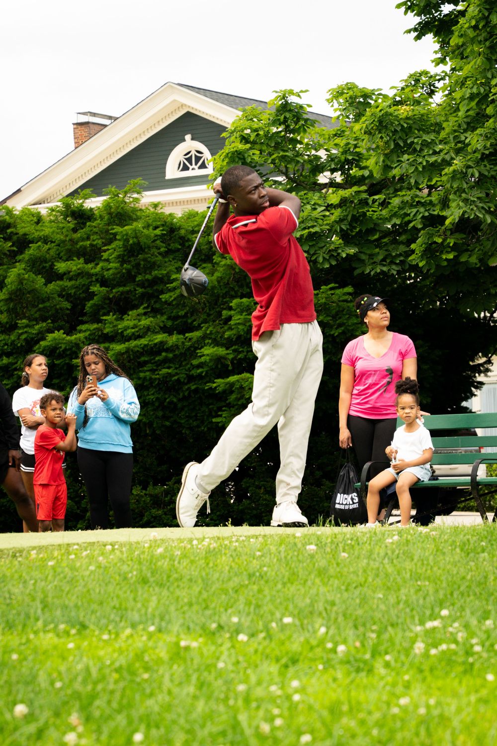 Group of people practicing tai chi exercises together on a lush green lawn near buildings on a sunny day.