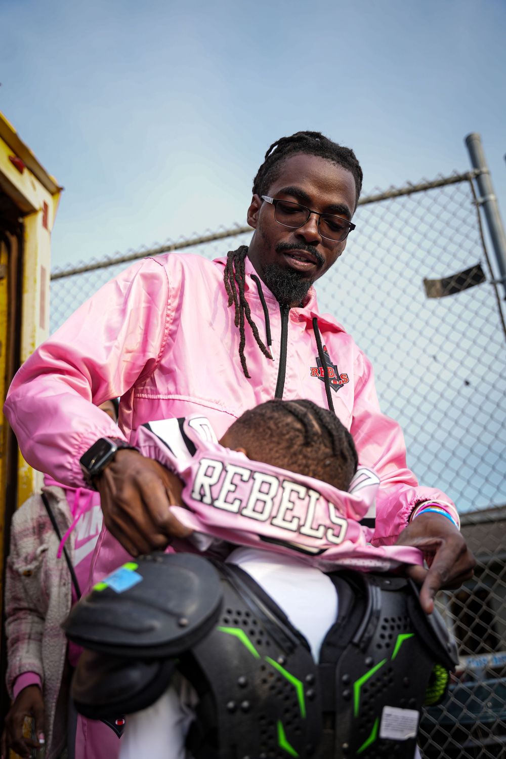 A person in a pink jacket poses with a black skateboard against a chain link fence in multiple sequential shots.