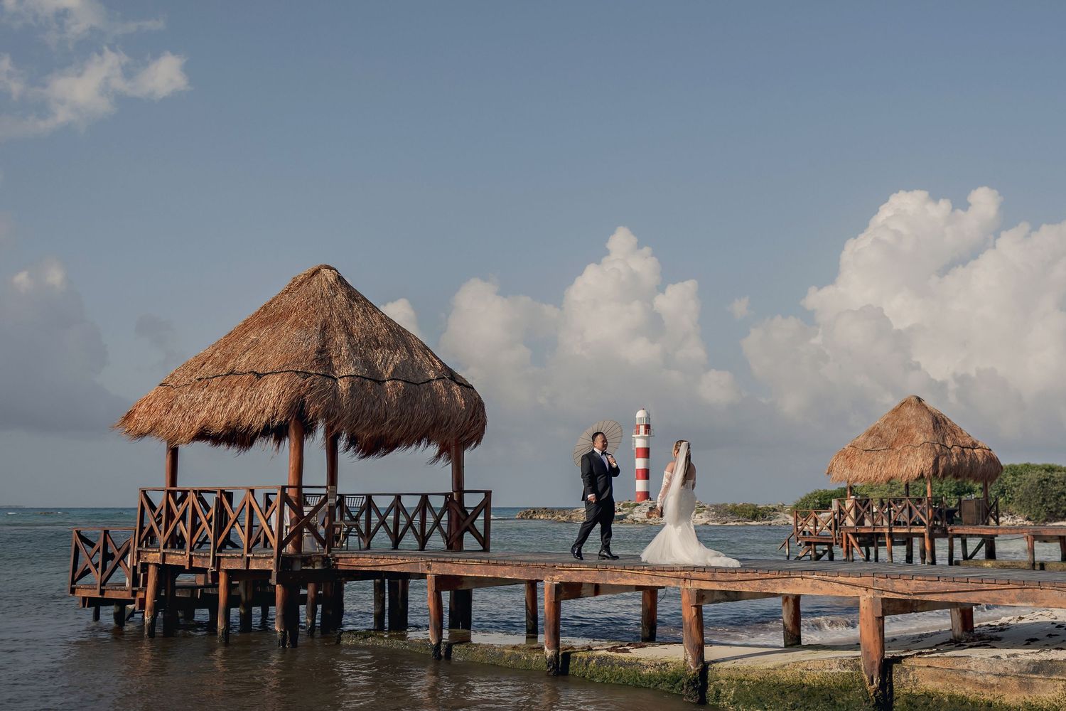 Bride and groom walking on a wooden pier at Hyatt Ziva Cancun with lighthouse in the background