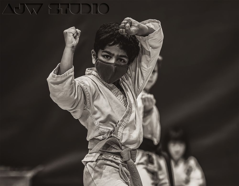 A martial artist in white karate uniform performs a dynamic movement with raised arms.