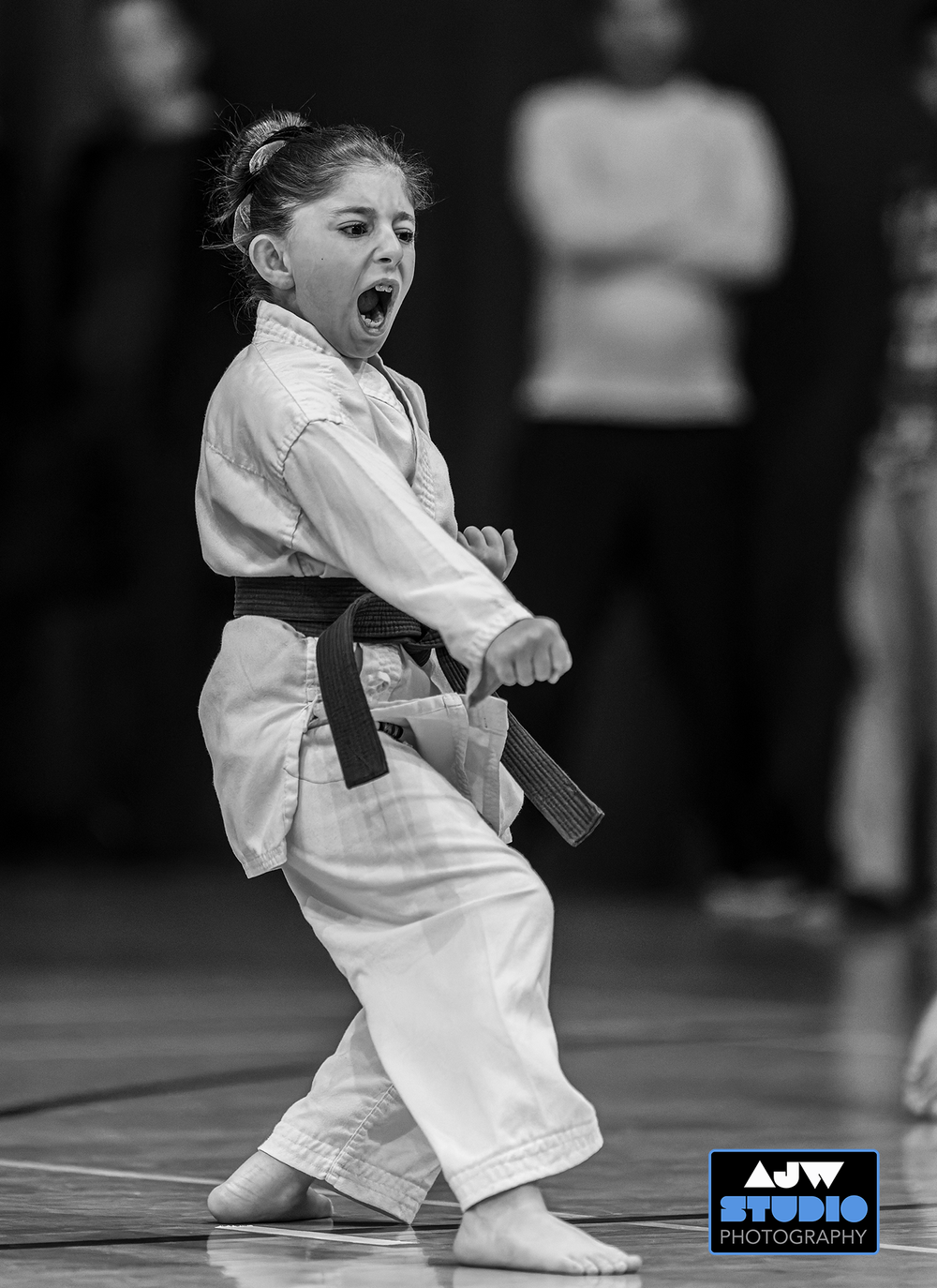 A young martial artist in white uniform performs a dramatic kata move during competition.