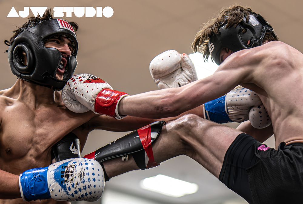 Two athletes engage in a kickboxing match wearing protective gear and throwing simultaneous strikes.