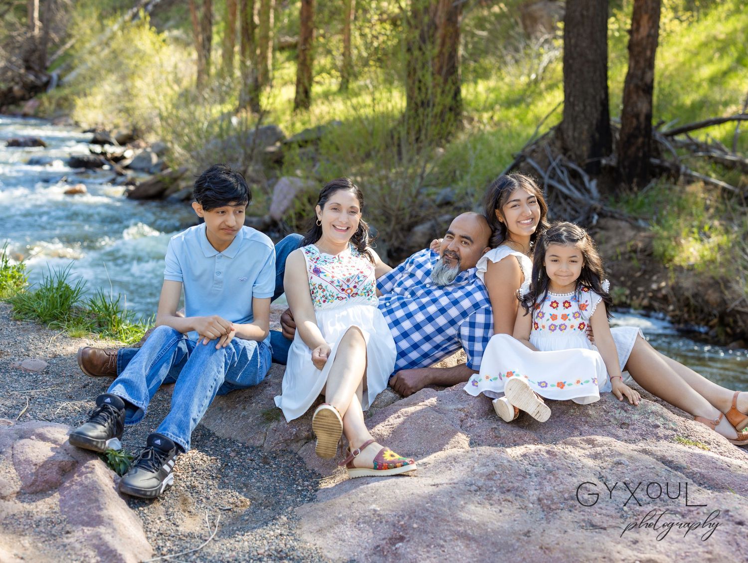 Group sits casually along riverbank enjoying nature and each other's company.