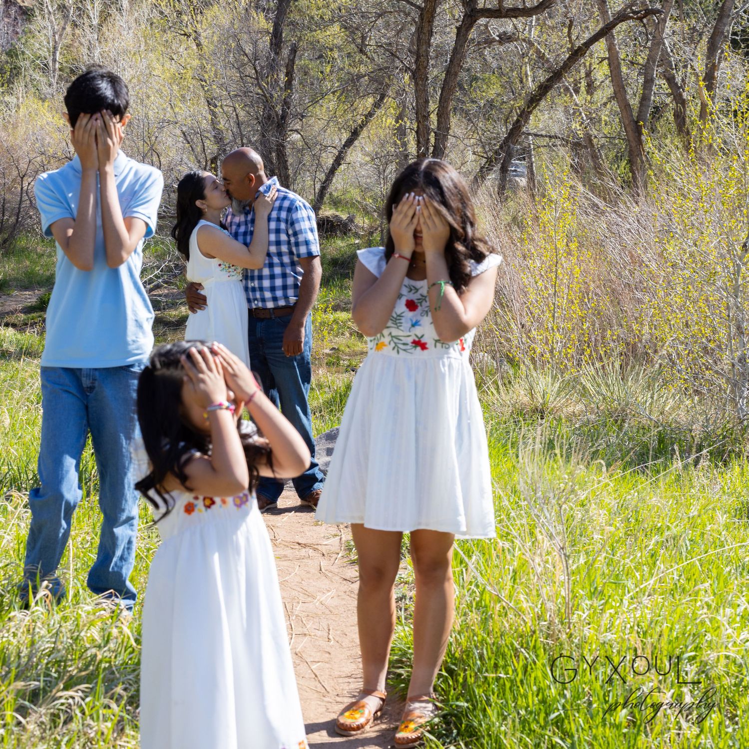 Group covering faces playfully during outdoor photoshoot by trail.