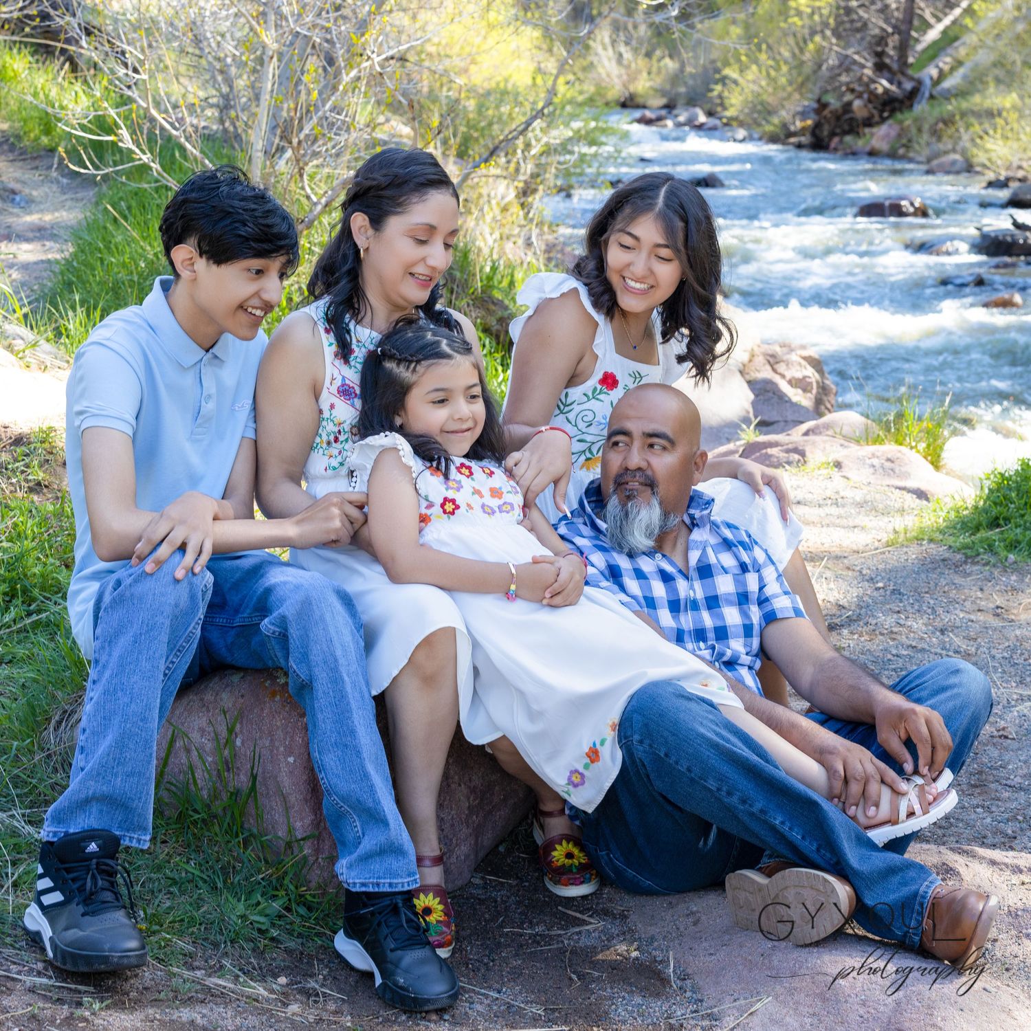 Group relaxes together on rocks beside flowing river in natural outdoor setting.