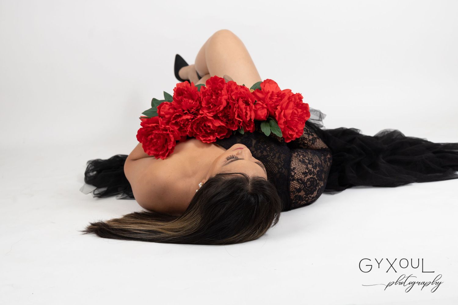 Artistic boudoir photo with red roses and black lace against white background.