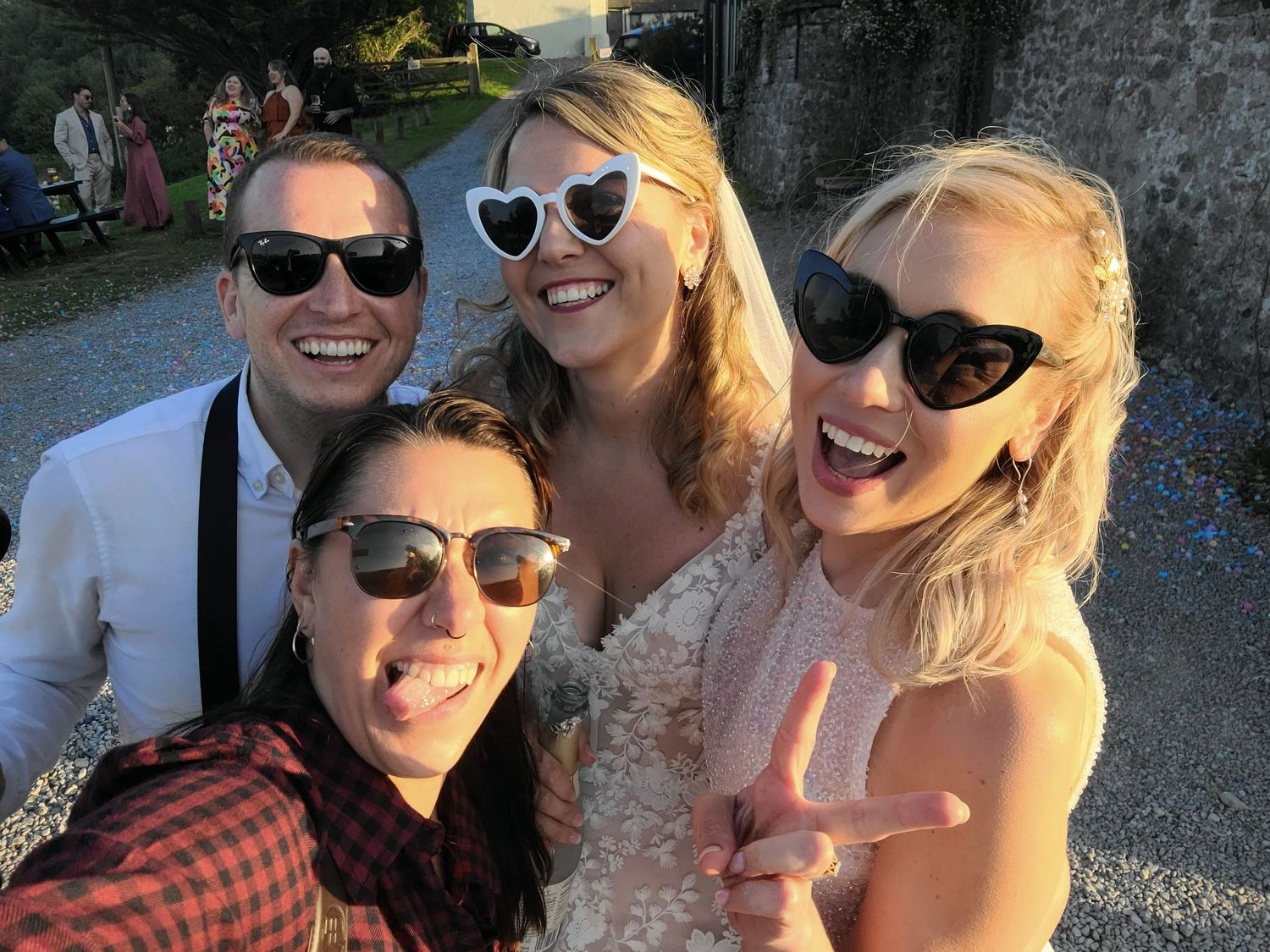 Wedding photographer and brides wearing sunglasses takes cheerful selfie outdoors.