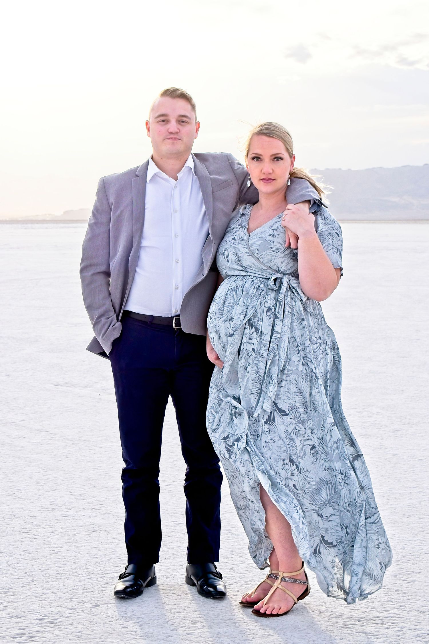 A young couple stands on the salt flats wearing a suit and a dress blowing in the wind