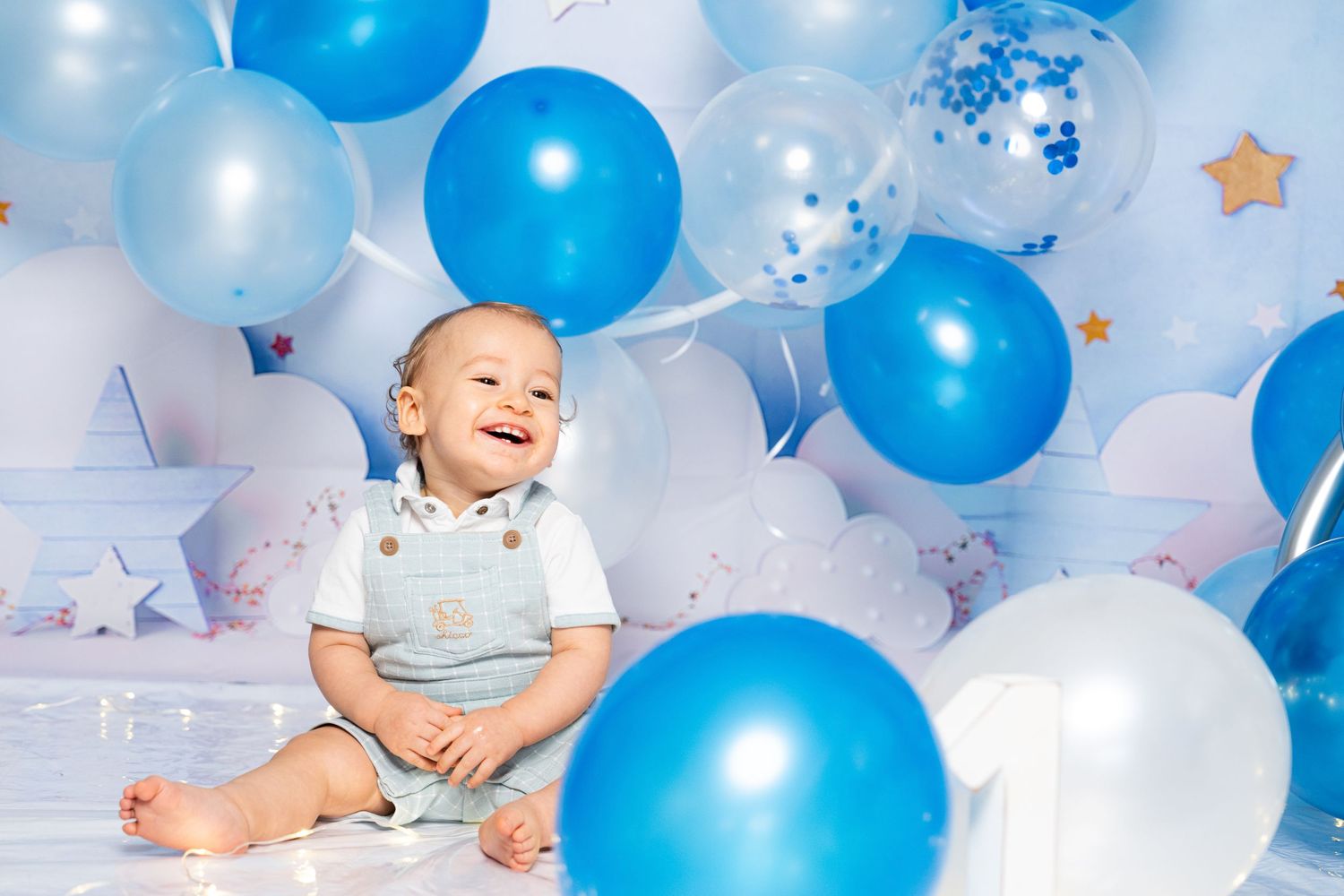 Baby playing with blue and white balloons against light blue backdrop.