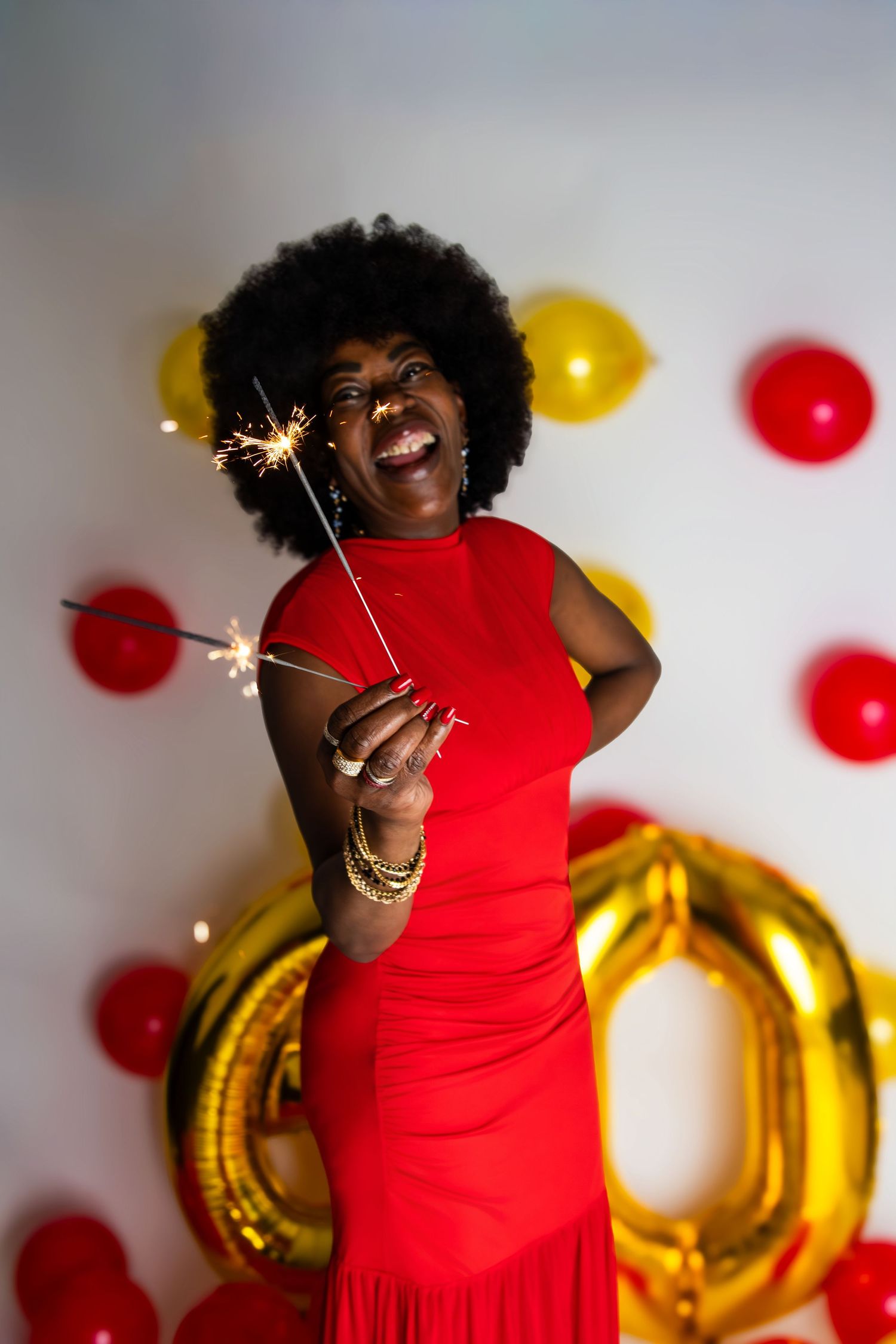 Woman in red dress celebrates with sparklers and festive balloons.
