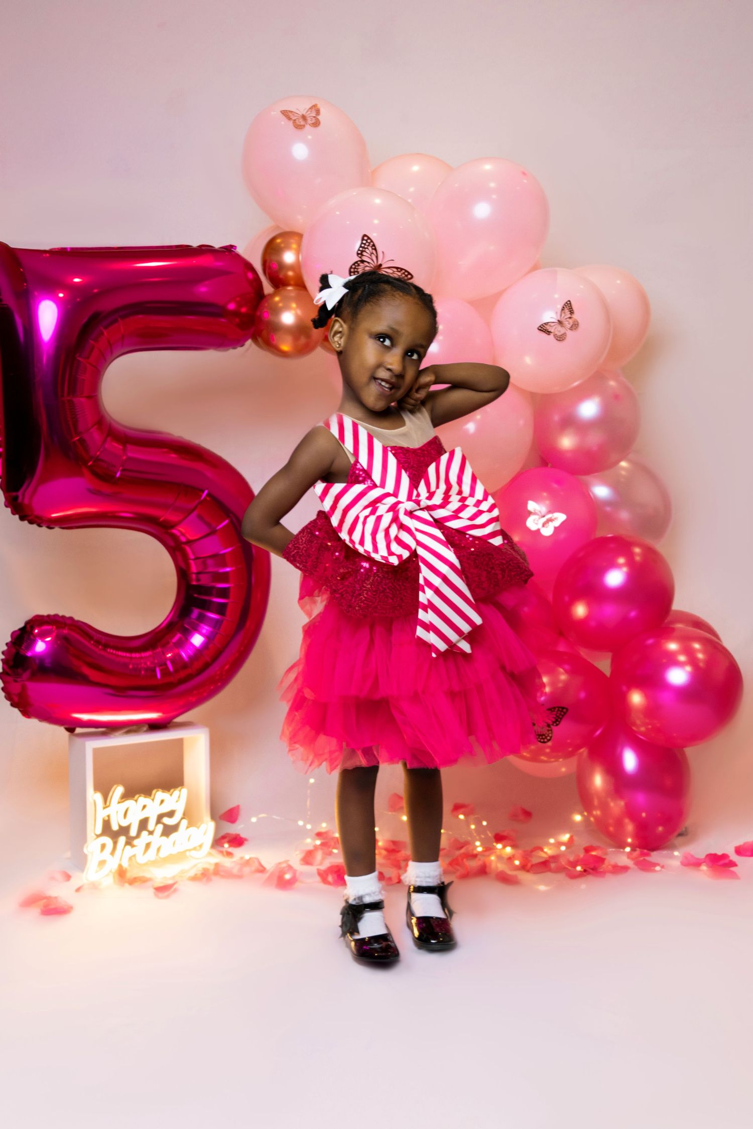 Pink and magenta balloon decorations with butterflies create a festive birthday setup against a white backdrop.