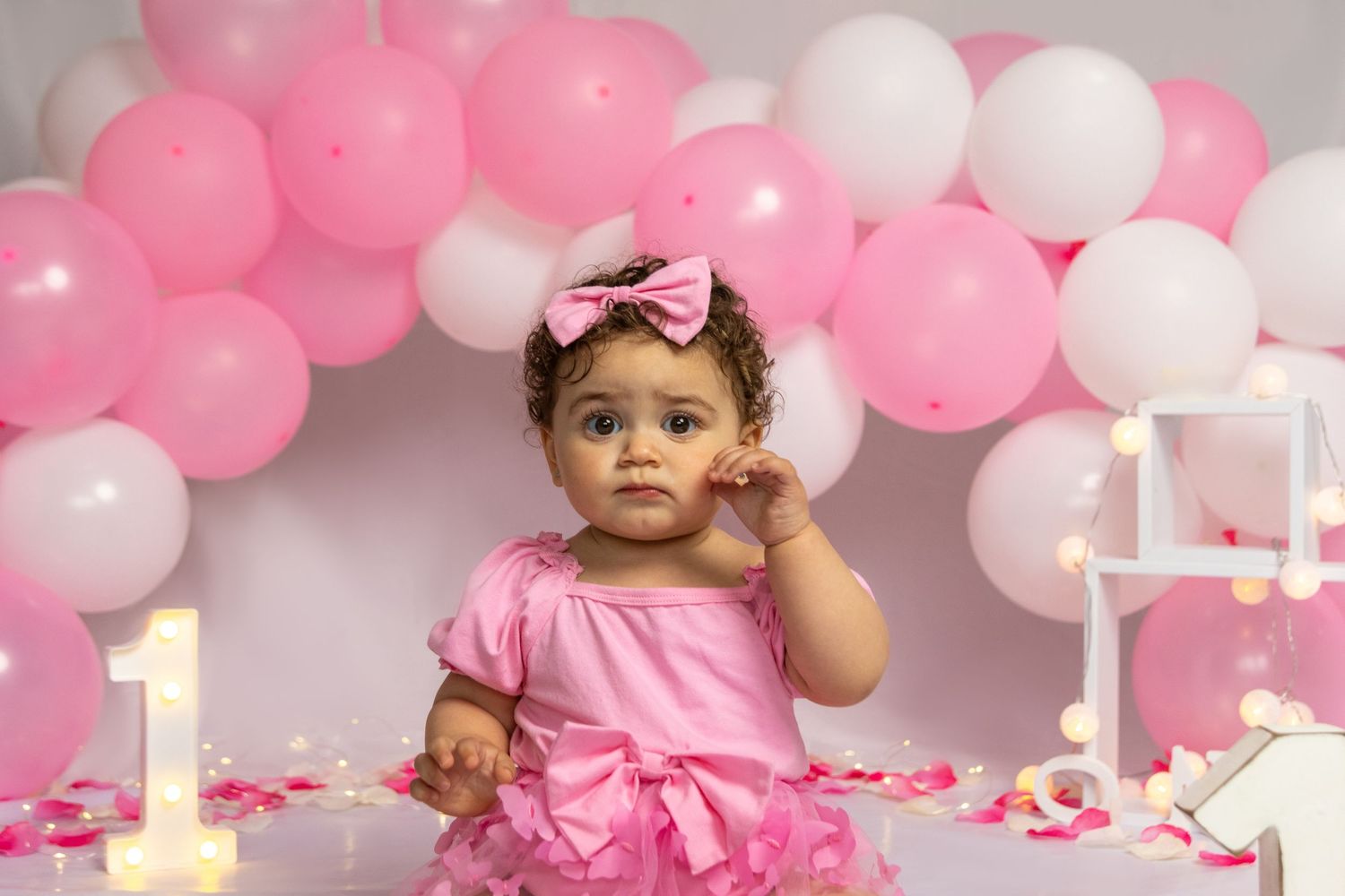 Baby in pink dress with balloons and number one decoration.