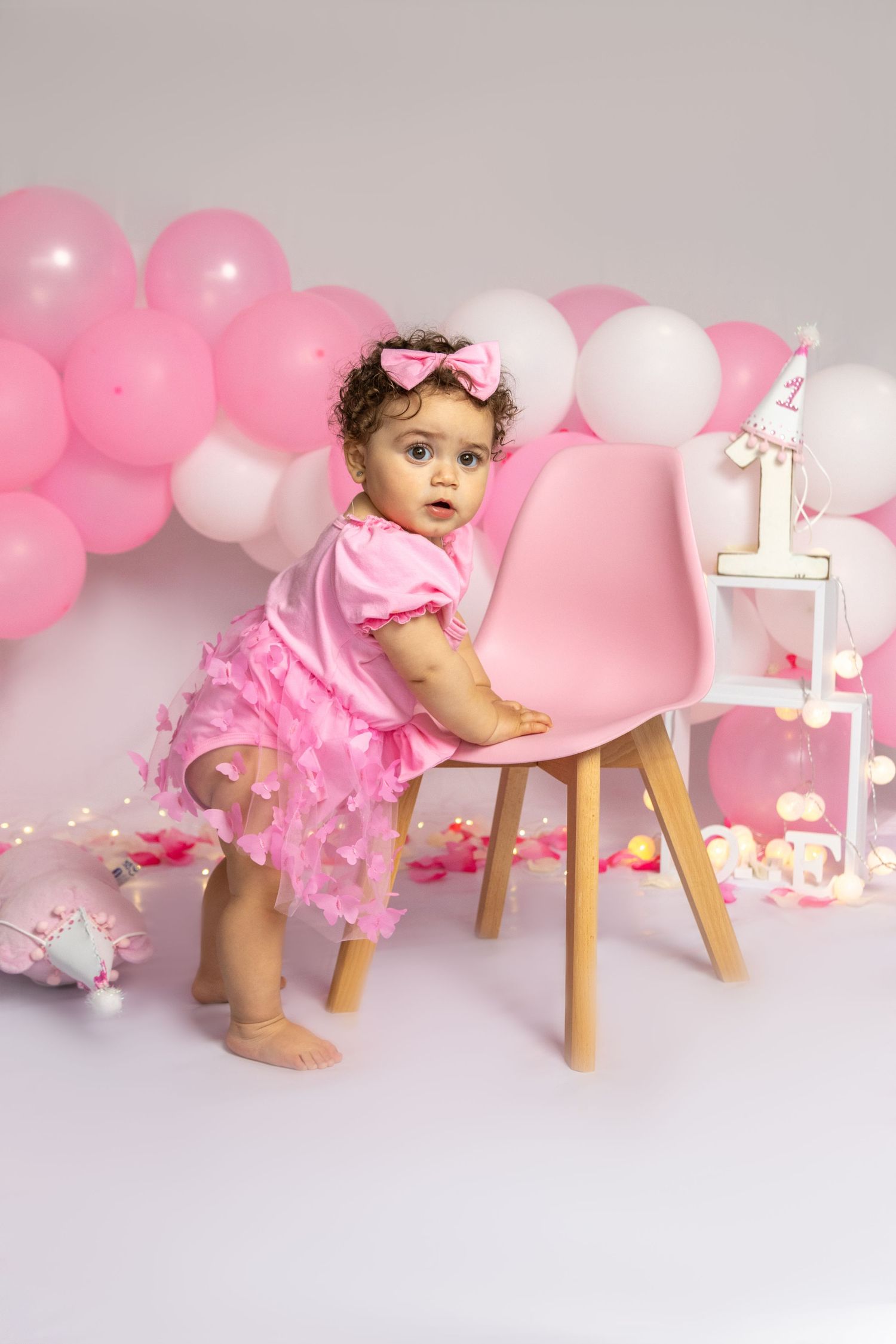 Birthday setup with wooden stool, pink balloons, and illuminated number one.