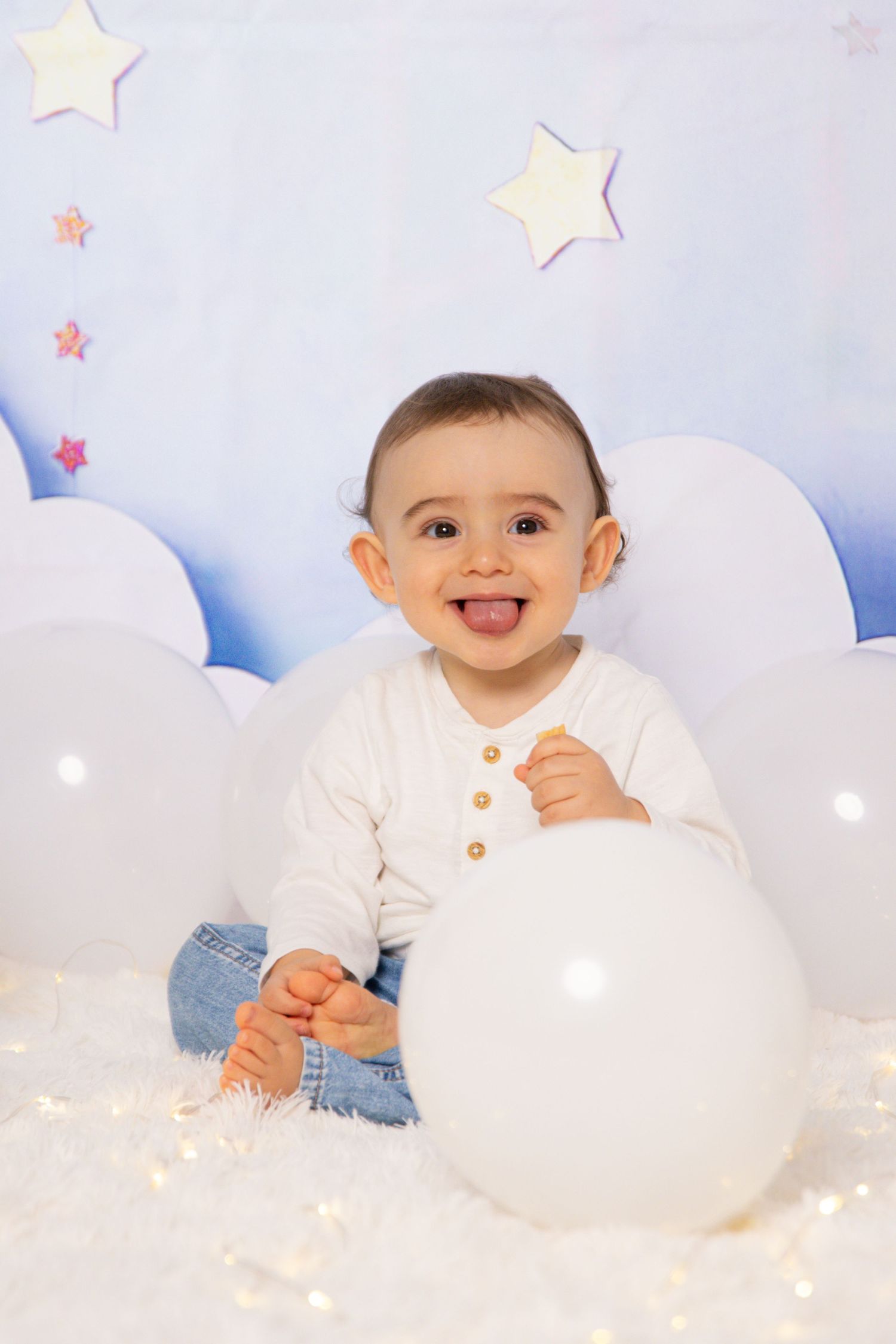 First birthday celebration setup with white balloons, cloud cutouts, and star decorations.
