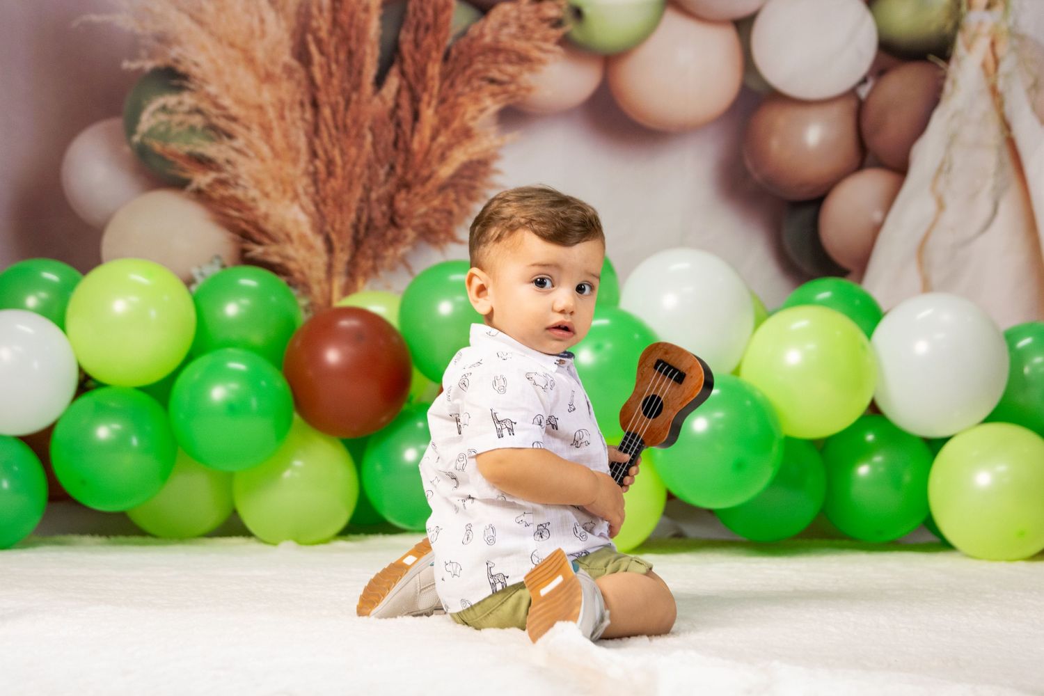 Birthday photo setup with green and white balloons and natural decorative elements.
