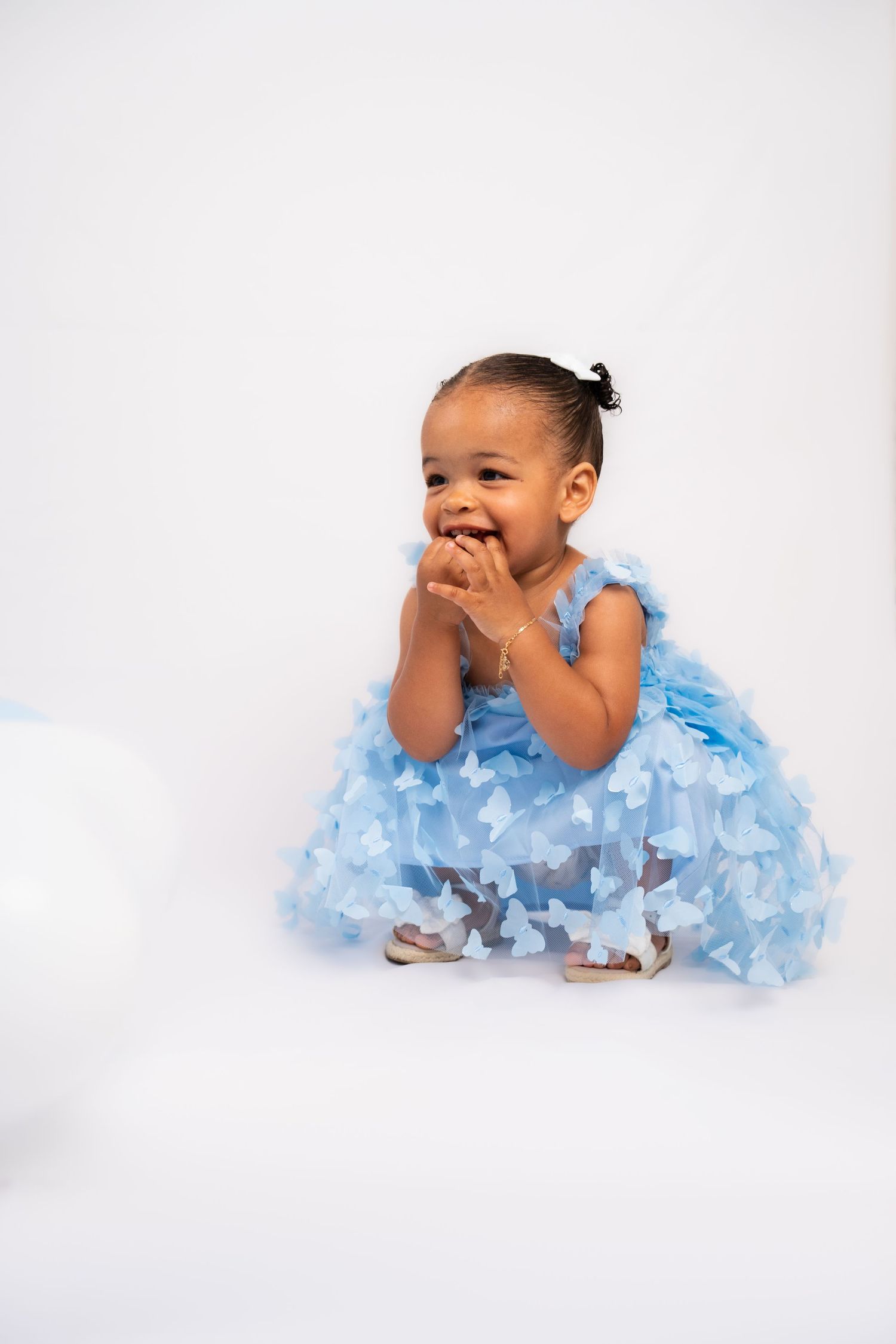 Joyful toddler in blue ruffled dress poses against white background.